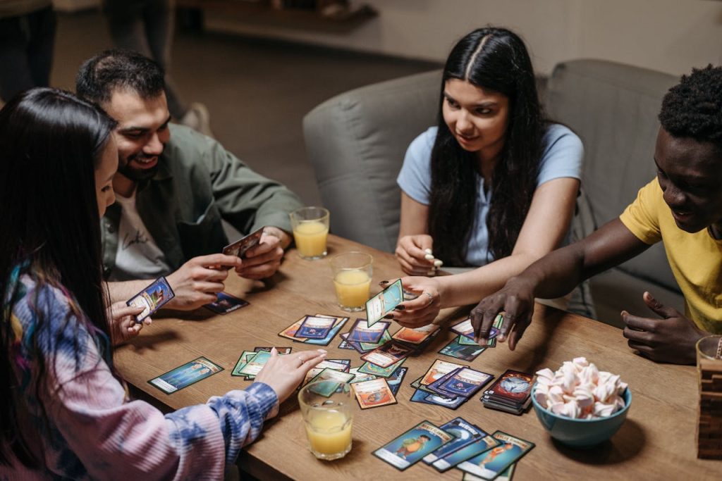 people-playing-cards-8111358 A diverse group of friends playing card games at a table with drinks, showcasing socialization and togetherness.